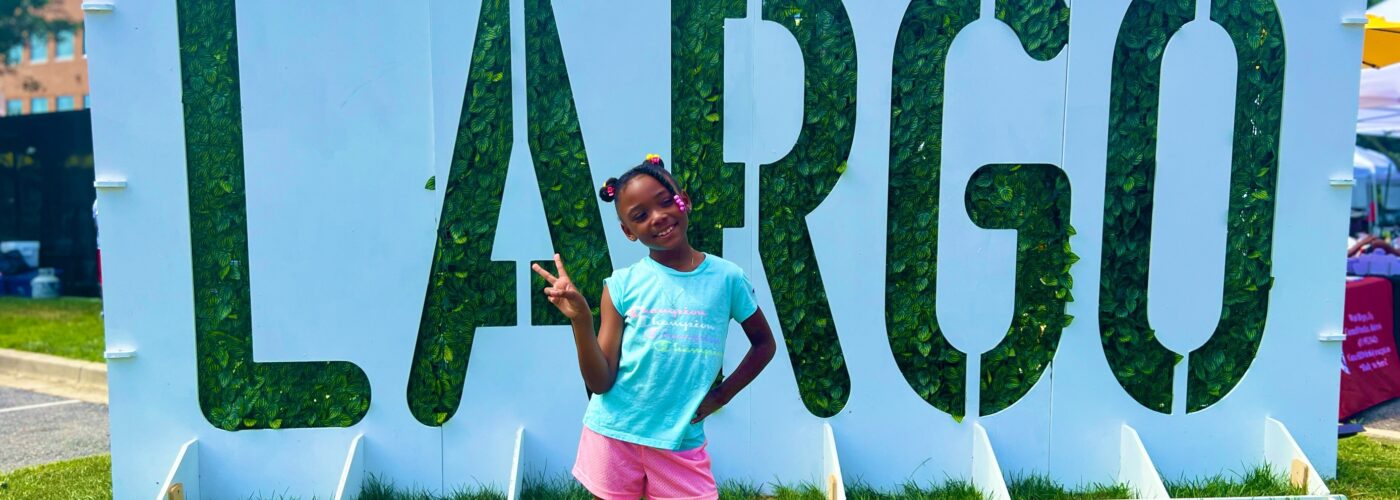 LARGO plant sign with black girl happily posing in front of it.