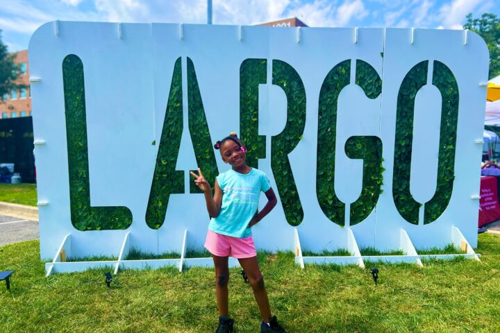 LARGO plant sign with black girl happily posing in front of it.