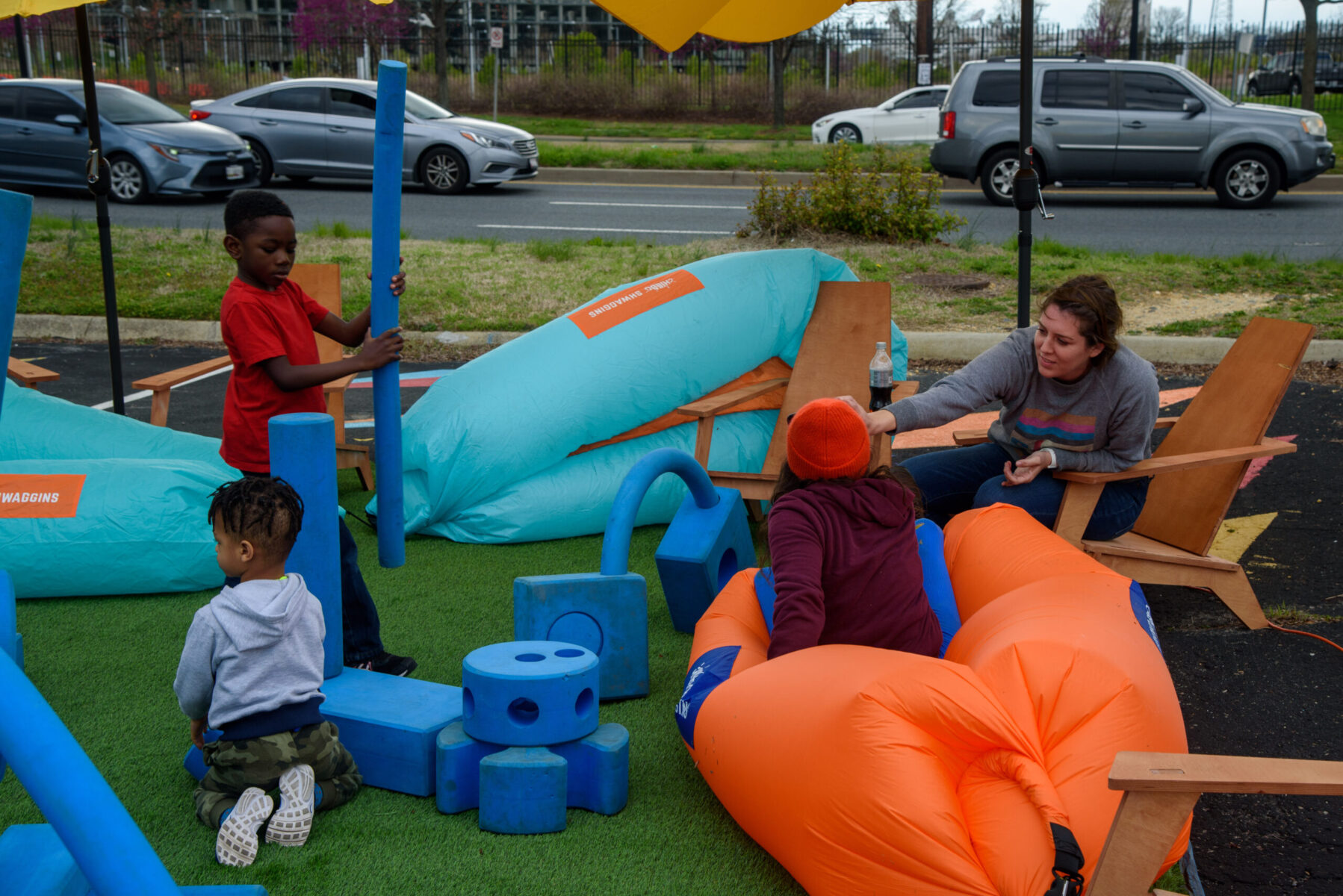Placemaking giant foam blocks for kids to play with and blowup chairs to sit in in a parking lot.