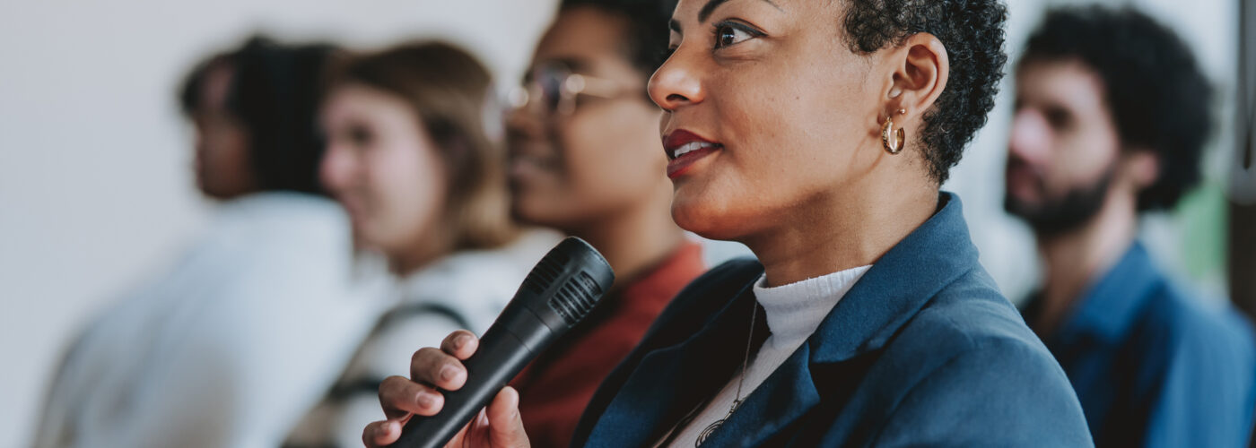 Register to speak: black woman speaking into a microphone at a meeting