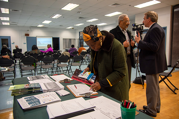 Woman standing next to table review planning documents at a community meeting.