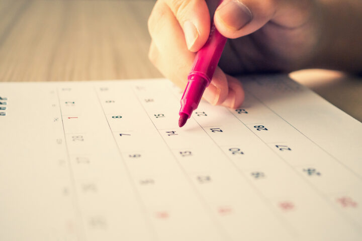 Hand holding pen and writing on a calendar.