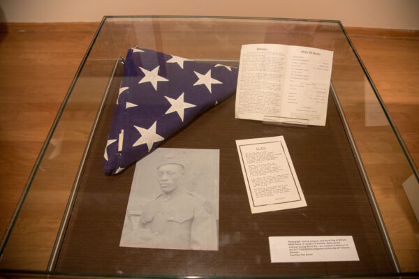 A display case with American flag, photo of an African-American soldier and a notebook.