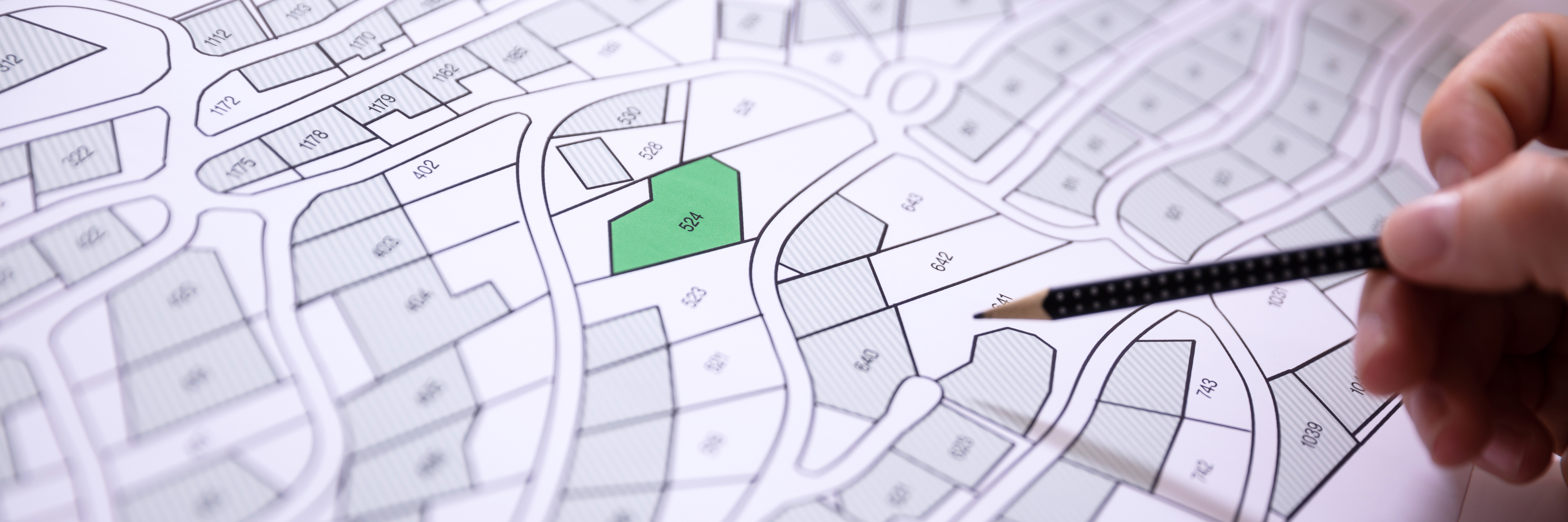 Human hand holding pencil over a subdivision development plan. One plot is highlighted in green. Image by AndreyPopov, istockphoto.com.