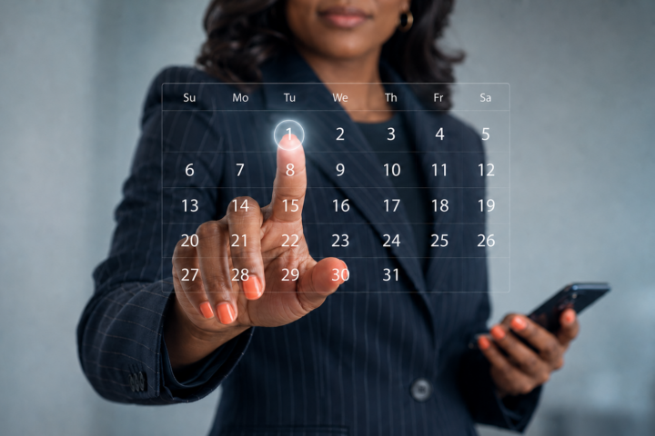 African American professional in a navy pinstriped suit selects a date on a transparent digital calendar while holding a smartphone.