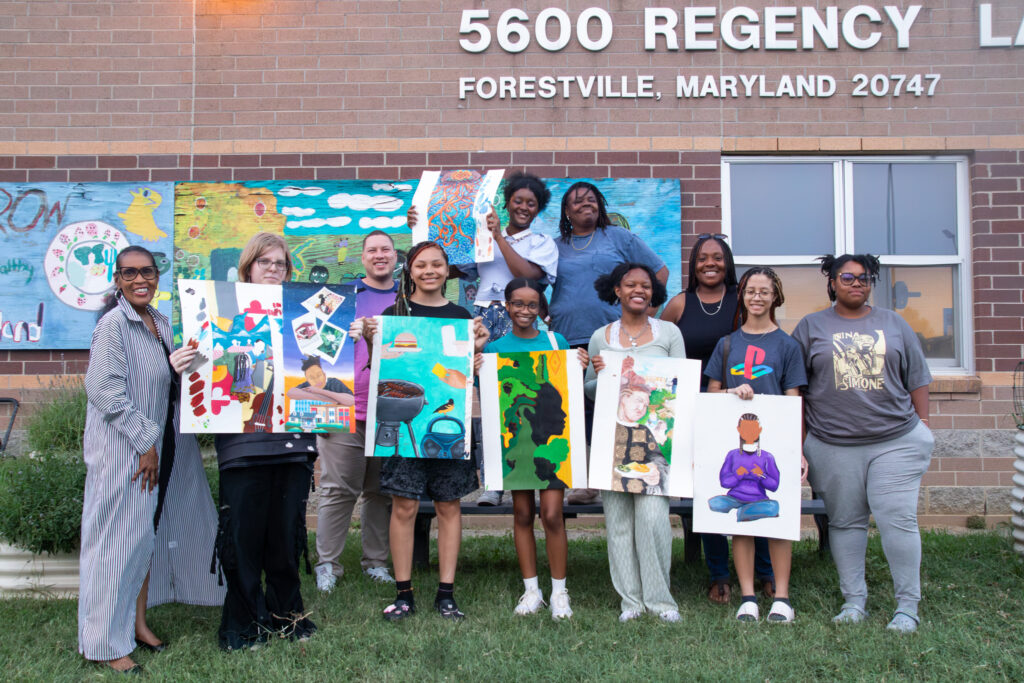 Students and facilitators pose outdoors, displaying colorful artwork created during Suitland student design sessions.