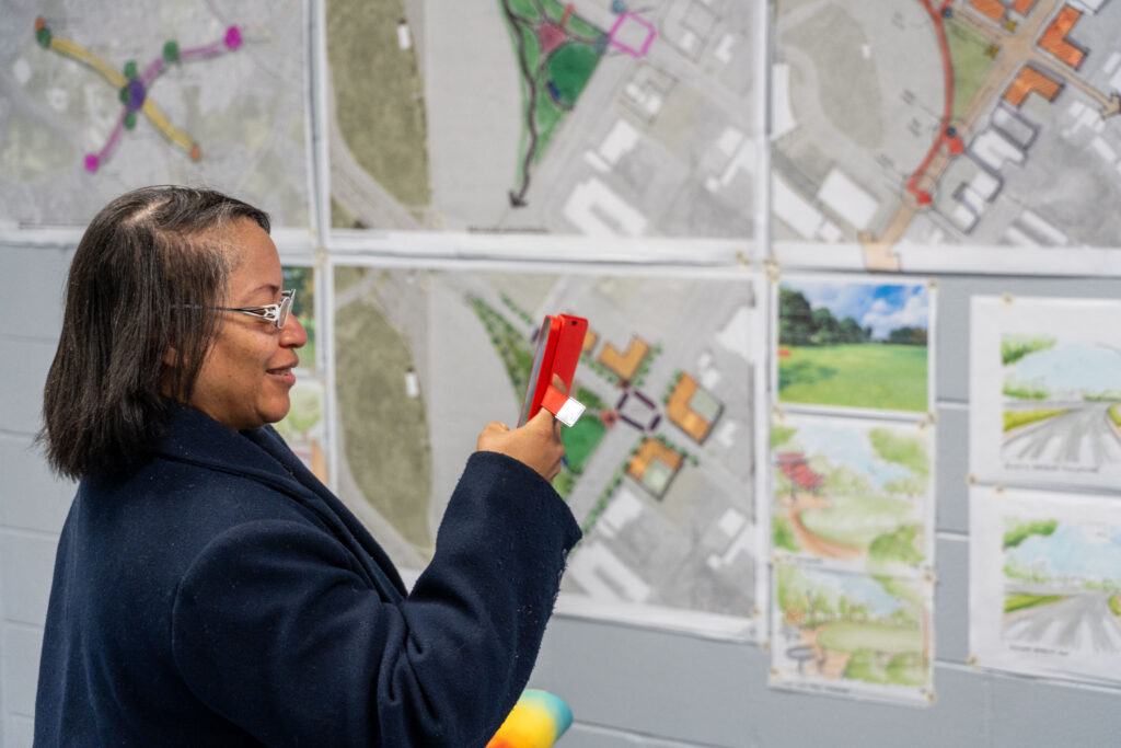 A participant photographs maps and design concepts displayed on a wall during a Suitland planning charrette.