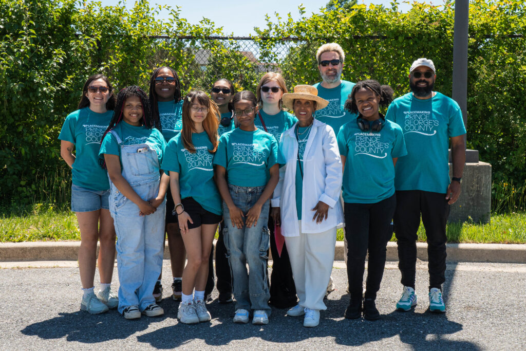 A group of students and M-NCPPC staff, many wearing matching teal shirts, poses outdoors at the Future Is Suitland celebration.