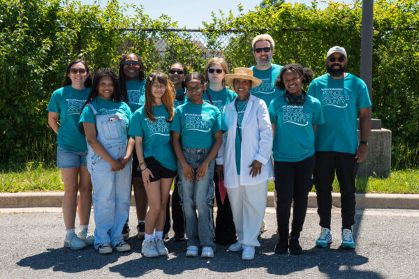 A group of students and M-NCPPC staff, many wearing matching teal shirts, poses outdoors at the Future Is Suitland celebration.