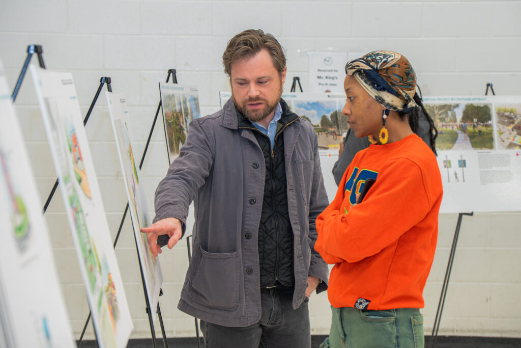 PGCPD Staff and one community engagement participant review and discuss design boards displayed on easels during a public planning event. Concept renderings and project information panels are visible throughout the exhibit space.